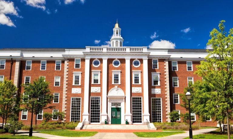 Harvard main building in brick and white paint with green landscaping and blue sky